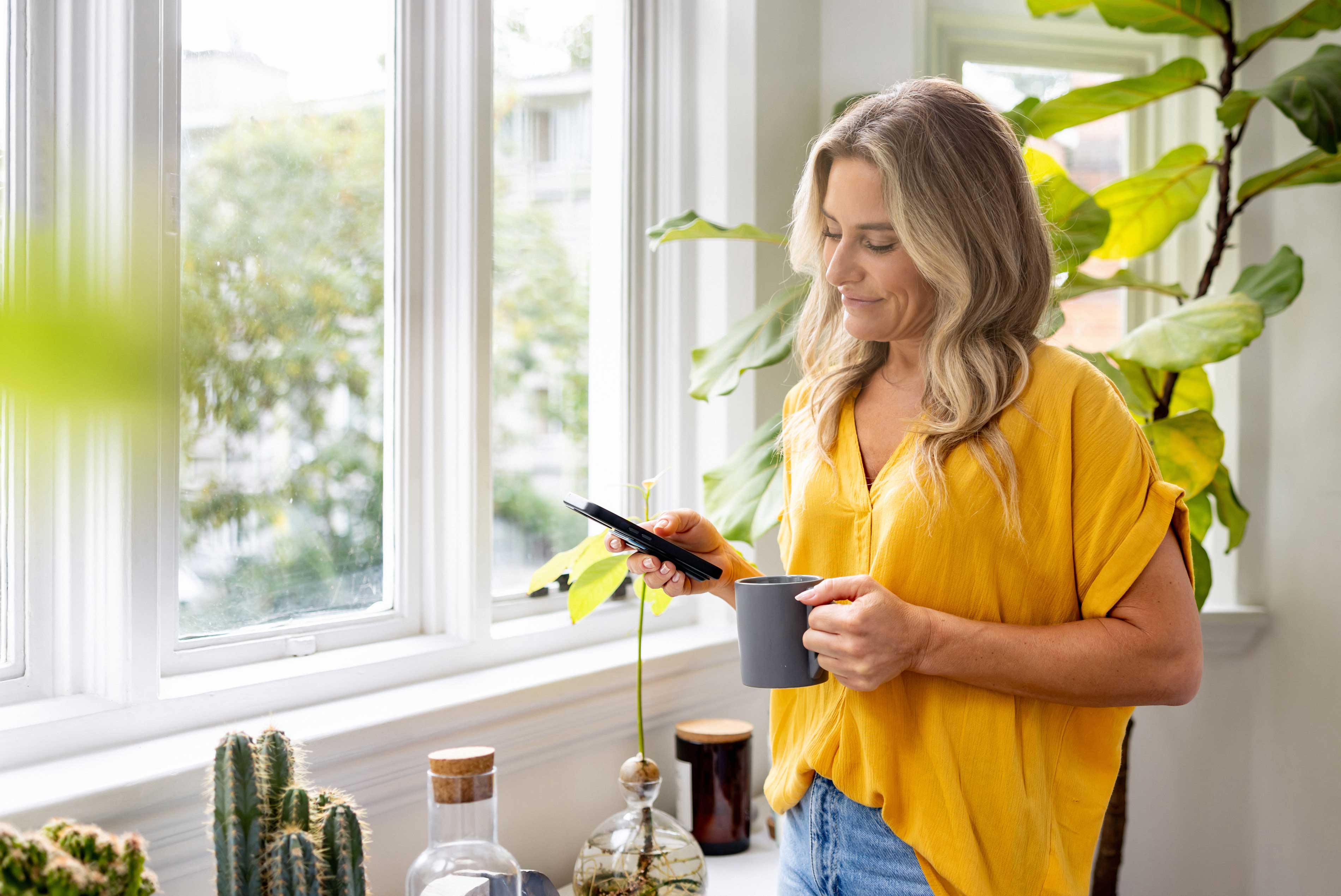Stock photo  Woman looking at social media on her cell phone while drinking coffee